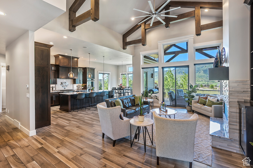 Living room with high vaulted ceiling, beam ceiling, light wood-style flooring, ceiling fan, and baseboards