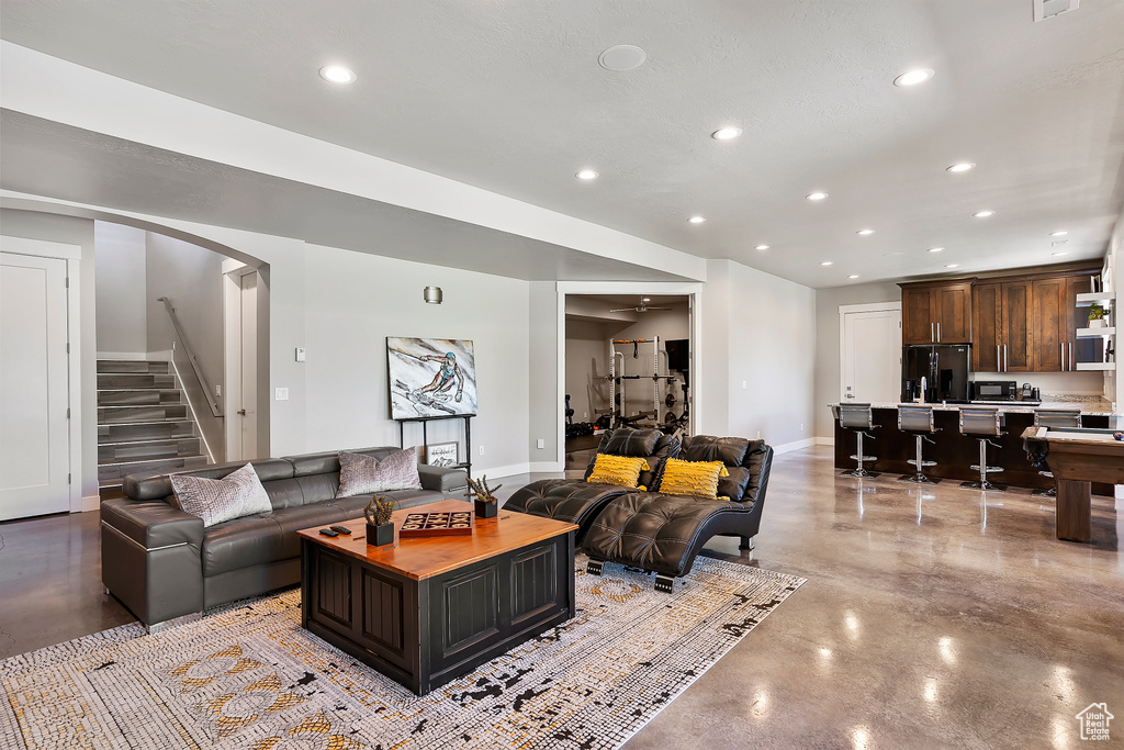 Living room with finished concrete floors, recessed lighting, stairs, arched walkways, and baseboards