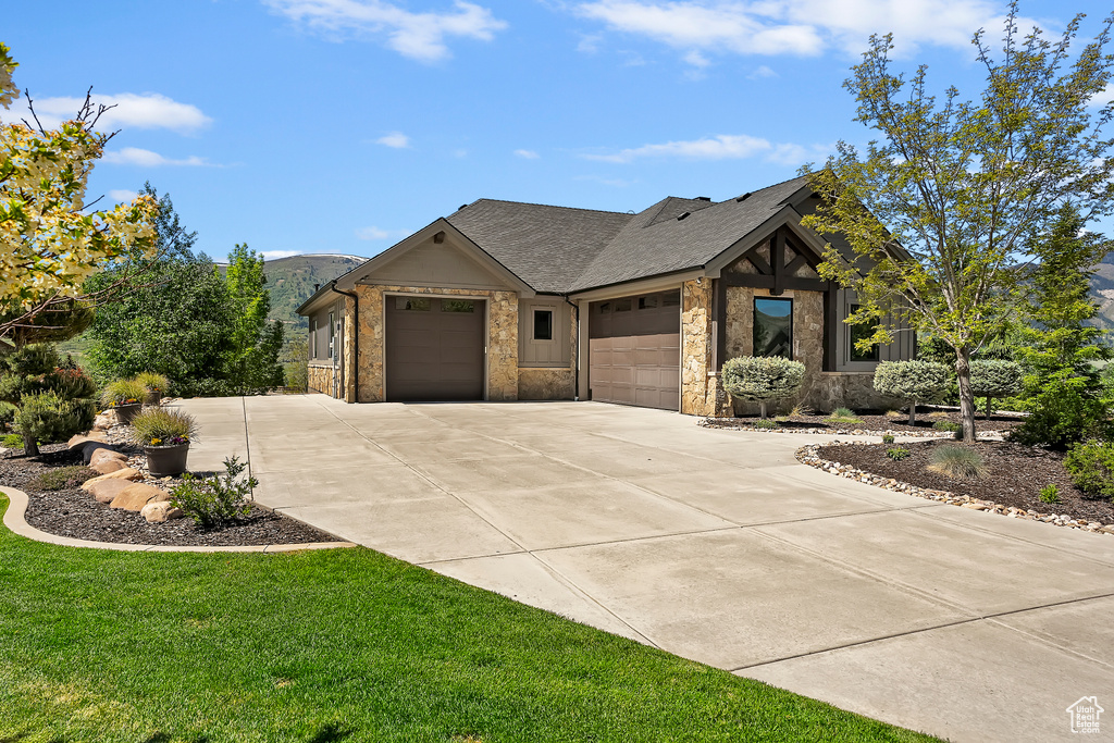 View of front facade featuring a garage, driveway, stone siding, and a front yard