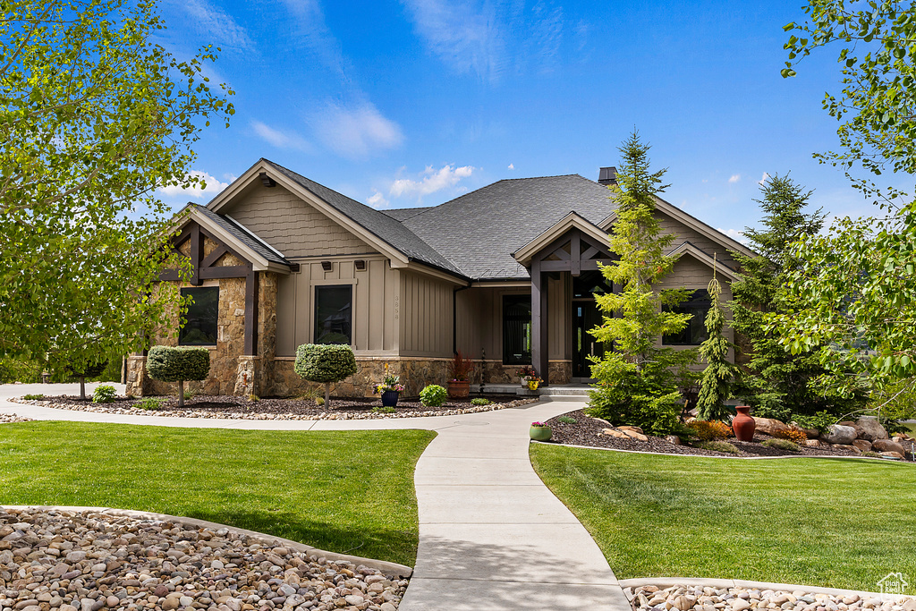 Craftsman house featuring board and batten siding, a front yard, stone siding, and roof with shingles