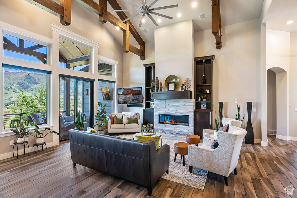 Living room featuring high vaulted ceiling, wood finished floors, a stone fireplace, baseboards, and beam ceiling