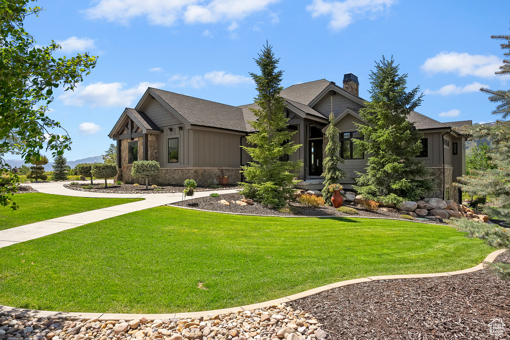 View of front of property with board and batten siding, a front lawn, a chimney, and a shingled roof