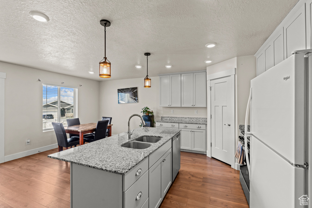 Kitchen featuring freestanding refrigerator, a sink, dishwasher, a textured ceiling, and recessed lighting