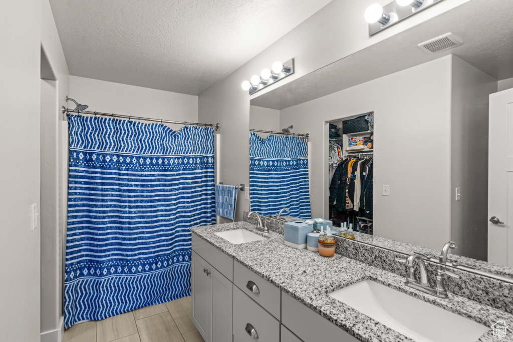 Full bathroom with double vanity, a textured ceiling, a shower with curtain, and a spacious closet
