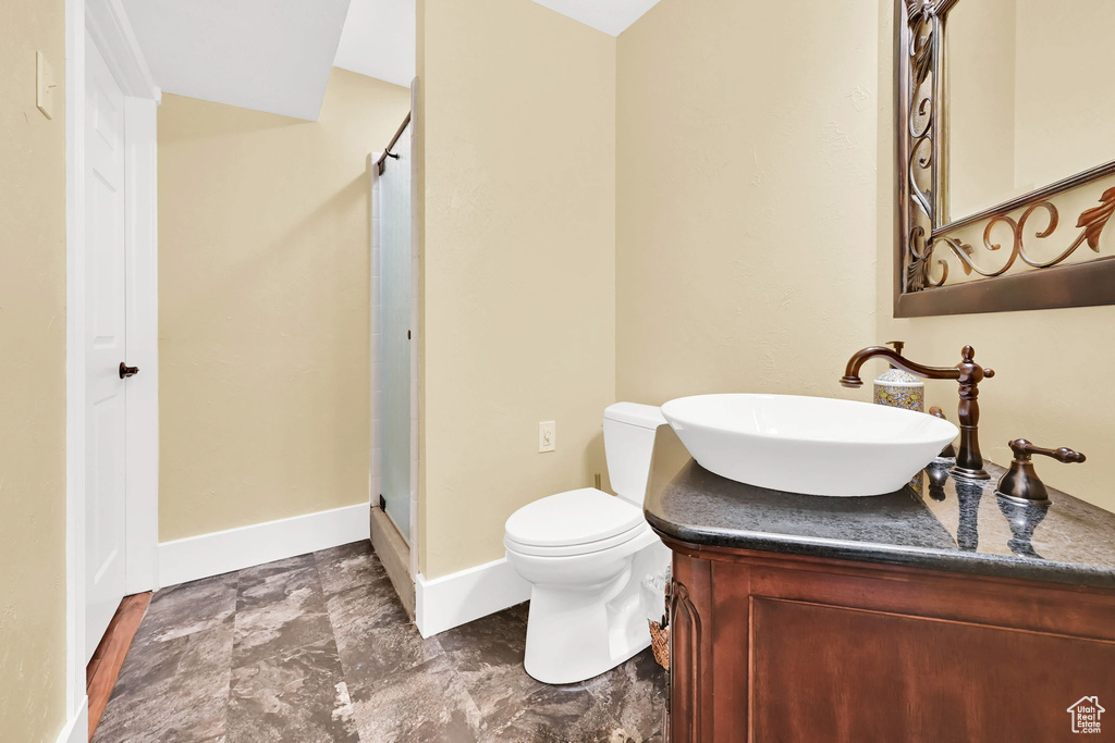 Bathroom featuring a shower stall, toilet, vanity, baseboards, and stone finish floors