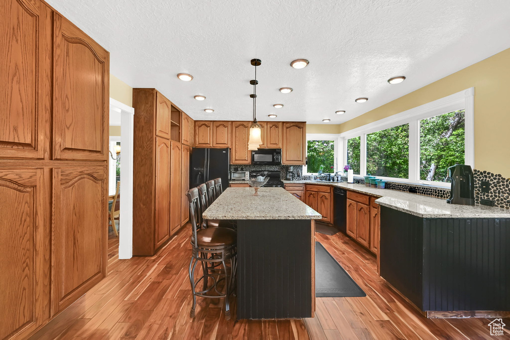 Kitchen featuring black appliances, decorative backsplash, a kitchen bar, a center island, and light wood-style floors