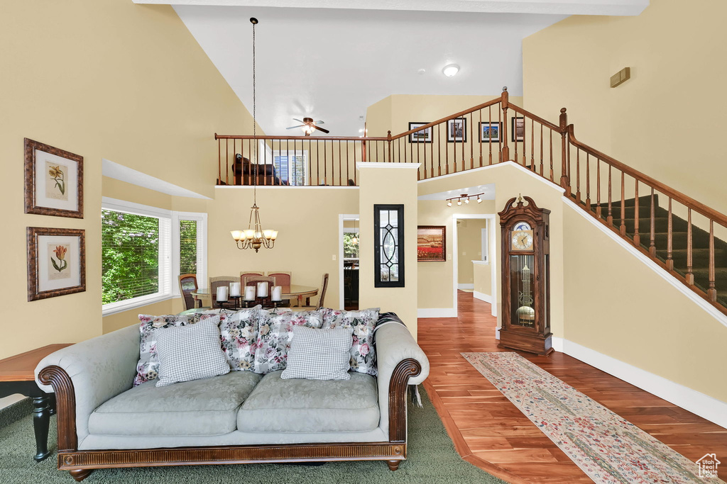 Living area with a towering ceiling, stairway, ceiling fan, a chandelier, and wood finished floors
