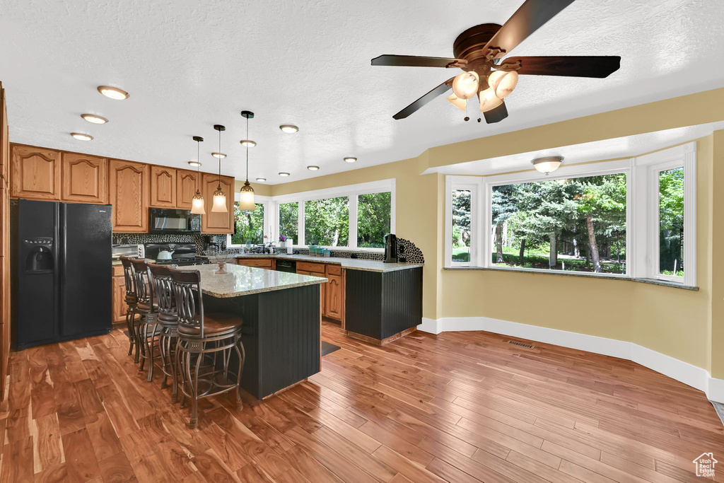 Kitchen with black appliances, brown cabinetry, baseboards, a ceiling fan, and a center island