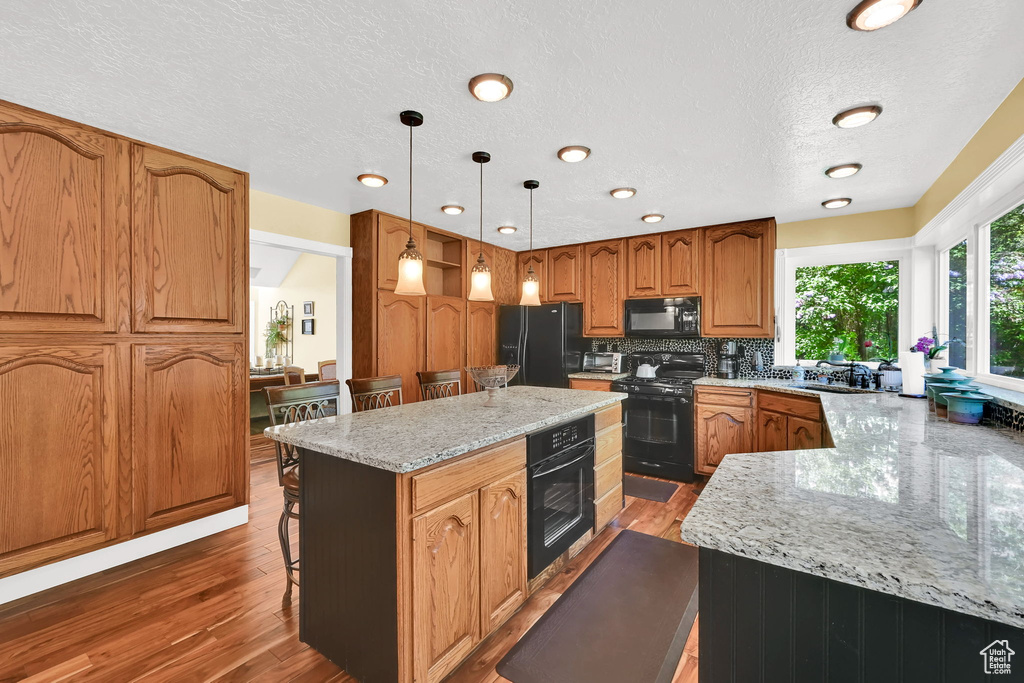 Kitchen with black appliances, light stone counters, a center island, a breakfast bar area, and a textured ceiling