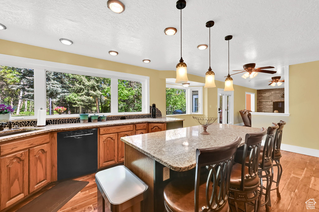 Kitchen with dishwasher, brown cabinetry, a kitchen island, a sink, and a ceiling fan