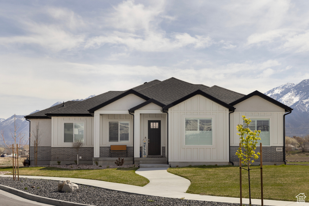 View of front of property featuring brick siding, a shingled roof, a mountain view, and a front yard