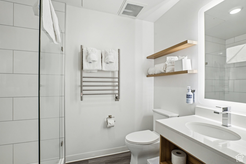 Full bath with radiator, toilet, vanity, wood finished floors, and a tile shower