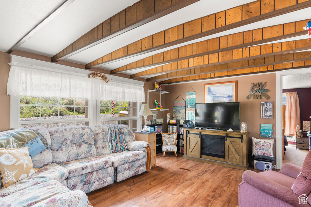 Living area with beam ceiling, wood finished floors, and a glass covered fireplace