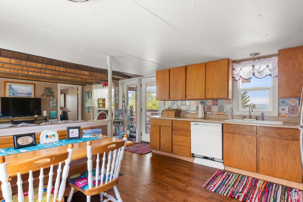 Kitchen with dishwasher, a sink, tasteful backsplash, dark wood-style flooring, and light countertops