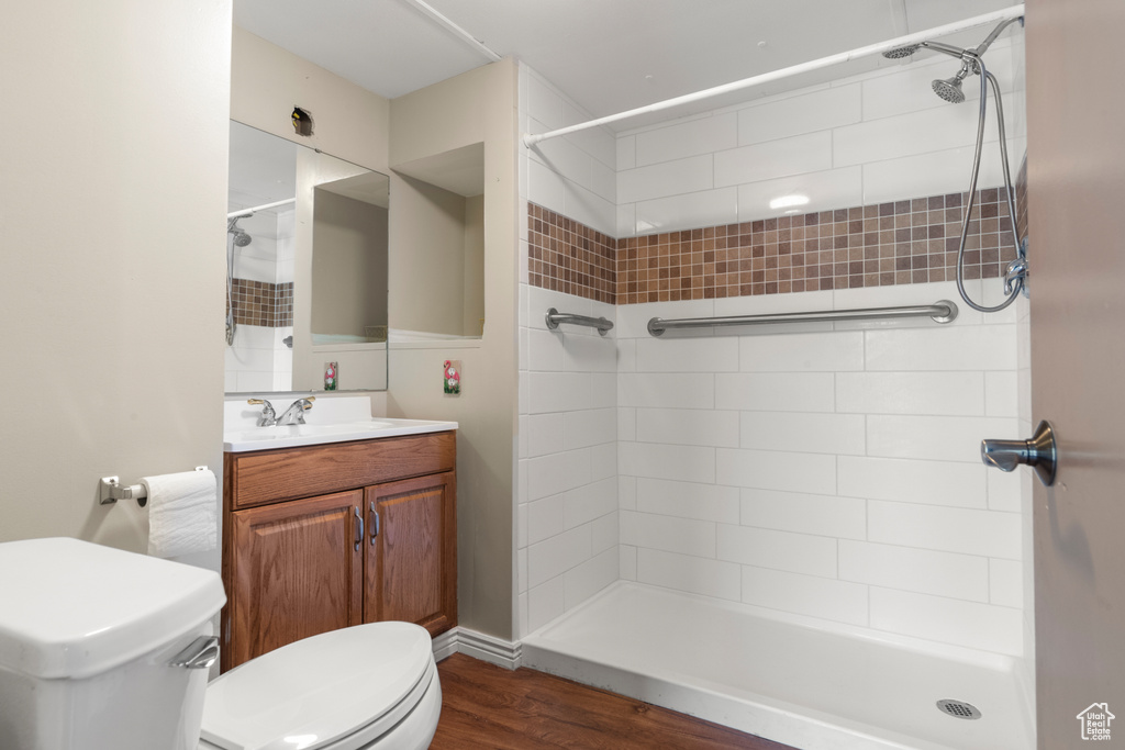 Bathroom featuring toilet, vanity, tiled shower, and wood finished floors