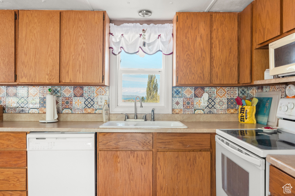 Kitchen with white appliances, a sink, light countertops, and decorative backsplash