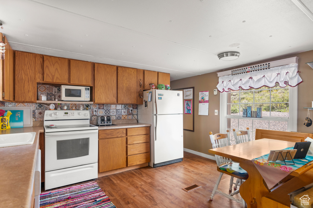 Kitchen with white appliances, backsplash, light wood-style flooring, brown cabinets, and light countertops
