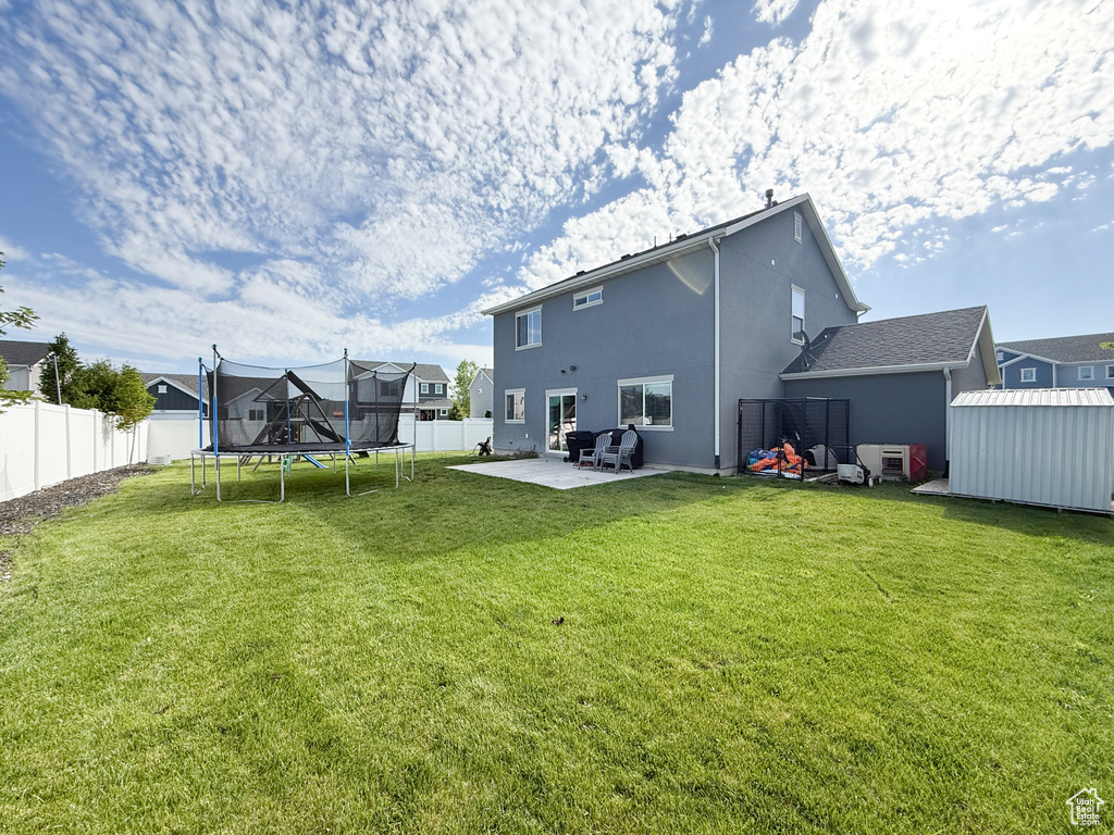 Back of house featuring a trampoline, a patio, stucco siding, and a residential view