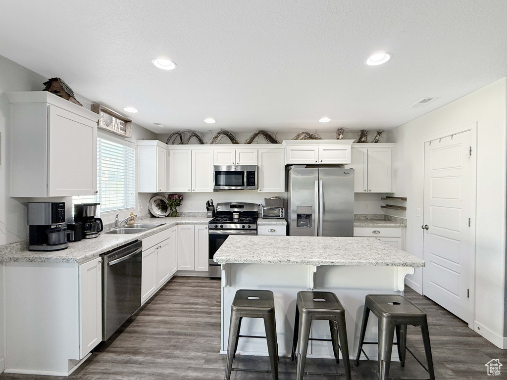 Kitchen featuring stainless steel appliances, a kitchen breakfast bar, a kitchen island, white cabinets, and a sink