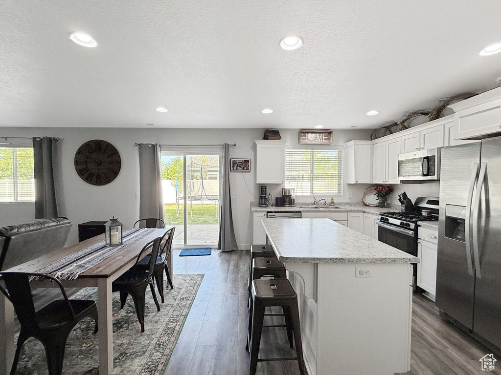Kitchen with appliances with stainless steel finishes, a sink, a center island, wood finished floors, and a breakfast bar area