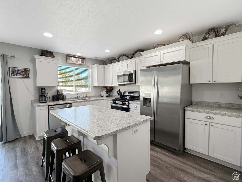 Kitchen featuring appliances with stainless steel finishes, a sink, a breakfast bar area, white cabinets, and light countertops
