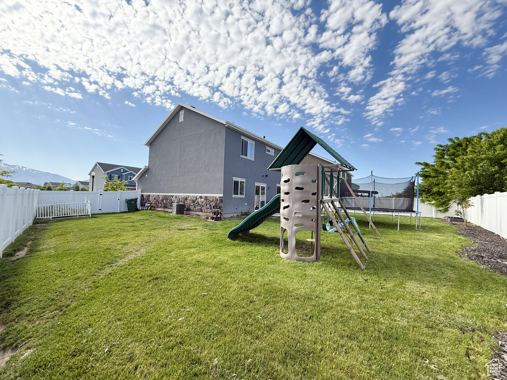 Rear view of house with a trampoline, a playground, stone siding, and stucco siding