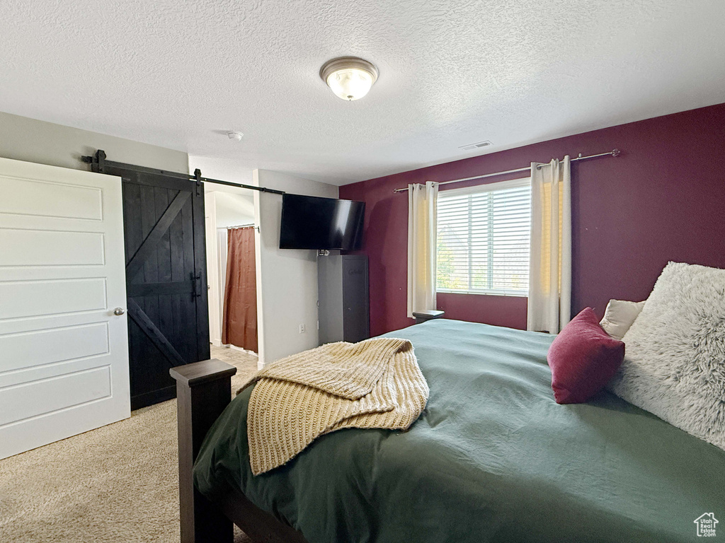 Bedroom with carpet flooring, a barn door, and a textured ceiling