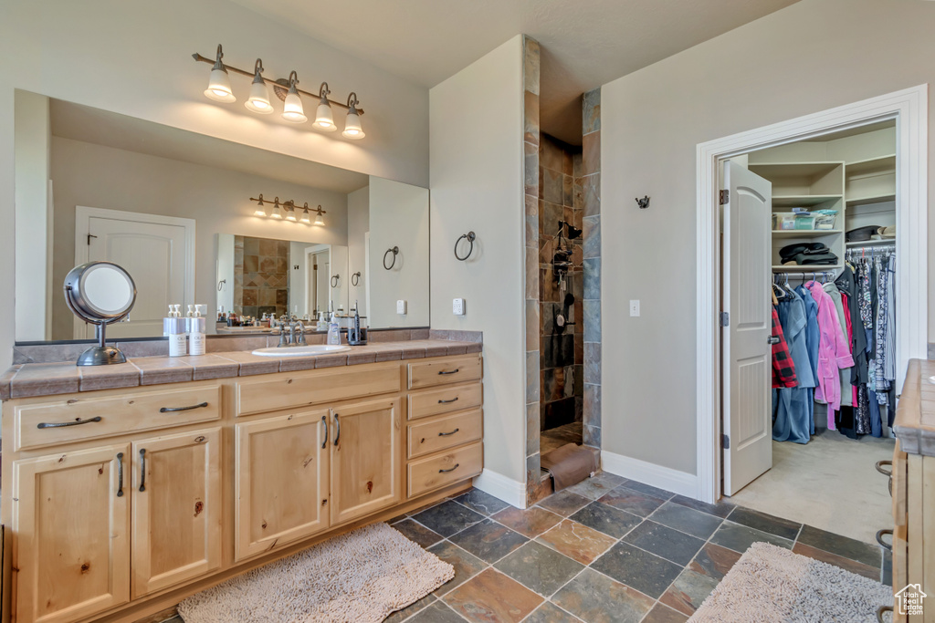 Full bathroom featuring walk in shower, stone tile floors, vanity, and baseboards