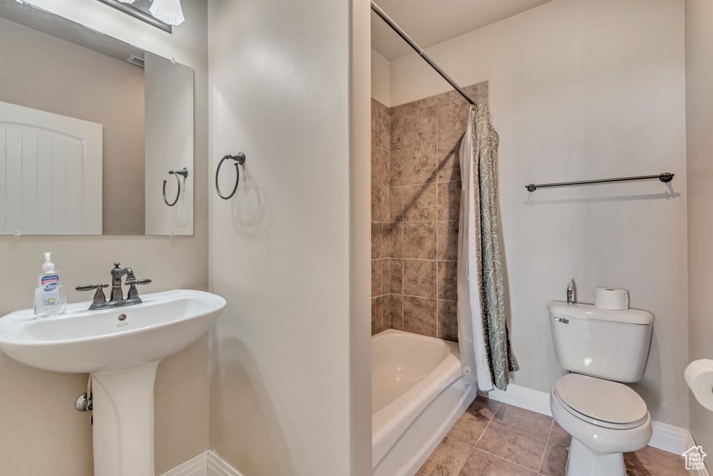 Full bathroom featuring toilet, shower / tub combo with curtain, baseboards, and a sink