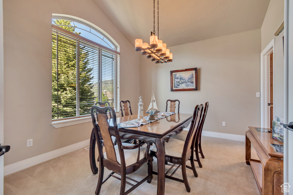 Dining area with light carpet, lofted ceiling, baseboards, and a chandelier