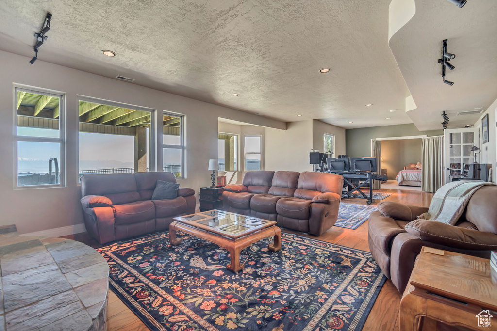 Living area with rail lighting, wood finished floors, recessed lighting, a textured ceiling, and baseboards