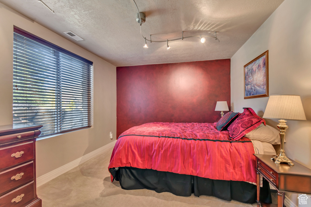Carpeted bedroom featuring baseboards, a textured ceiling, and an accent wall