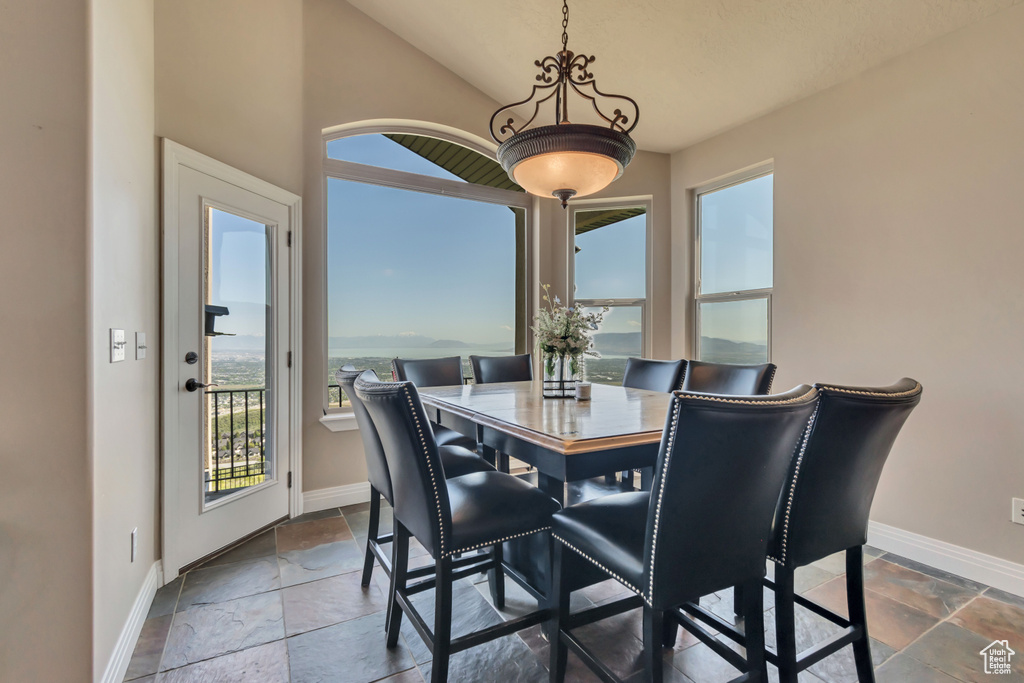 Dining room with baseboards, stone tile flooring, healthy amount of natural light, and vaulted ceiling
