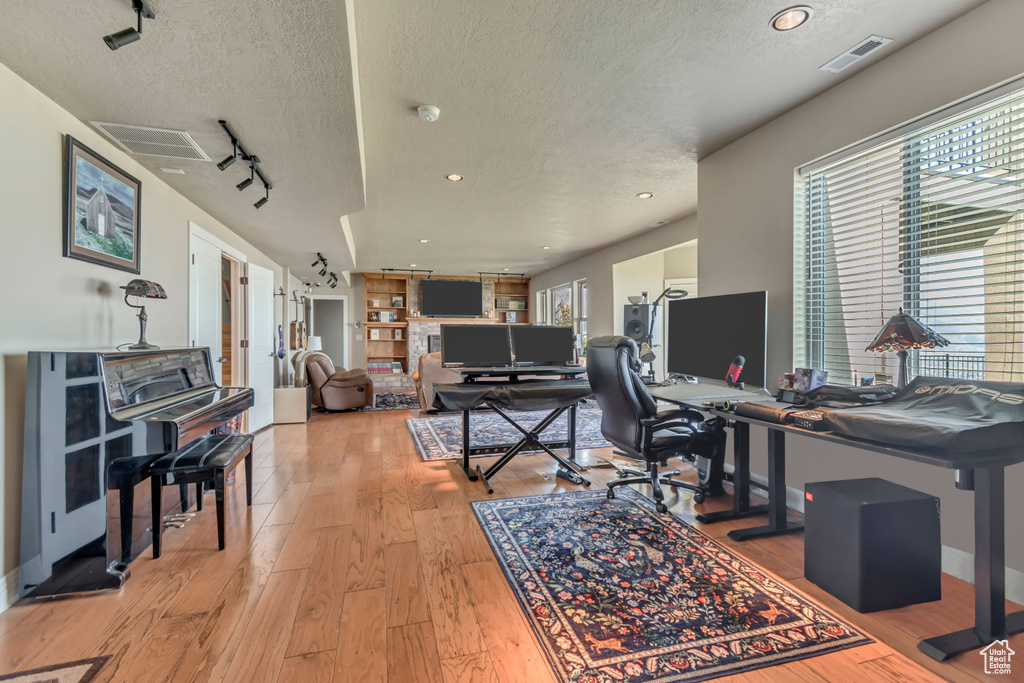 Office with a textured ceiling, light wood-type flooring, plenty of natural light, track lighting, and baseboards