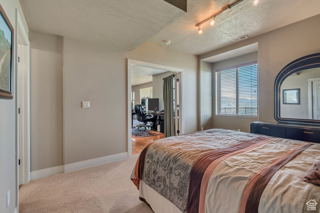 Bedroom with carpet floors, a textured ceiling, a desk, baseboards, and track lighting