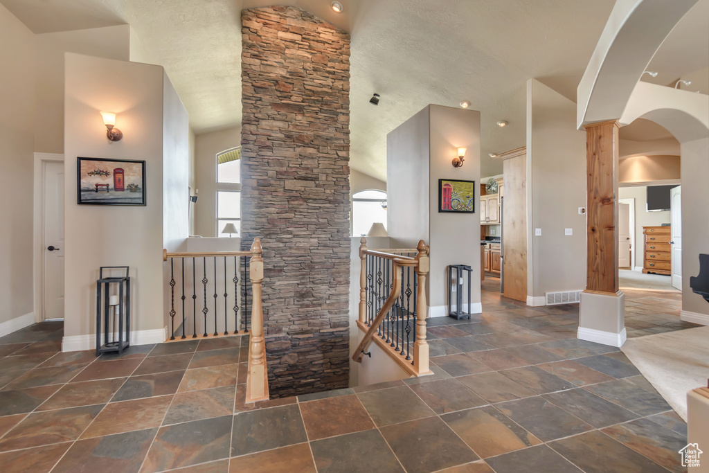 Foyer with arched walkways, baseboards, stone tile floors, and high vaulted ceiling