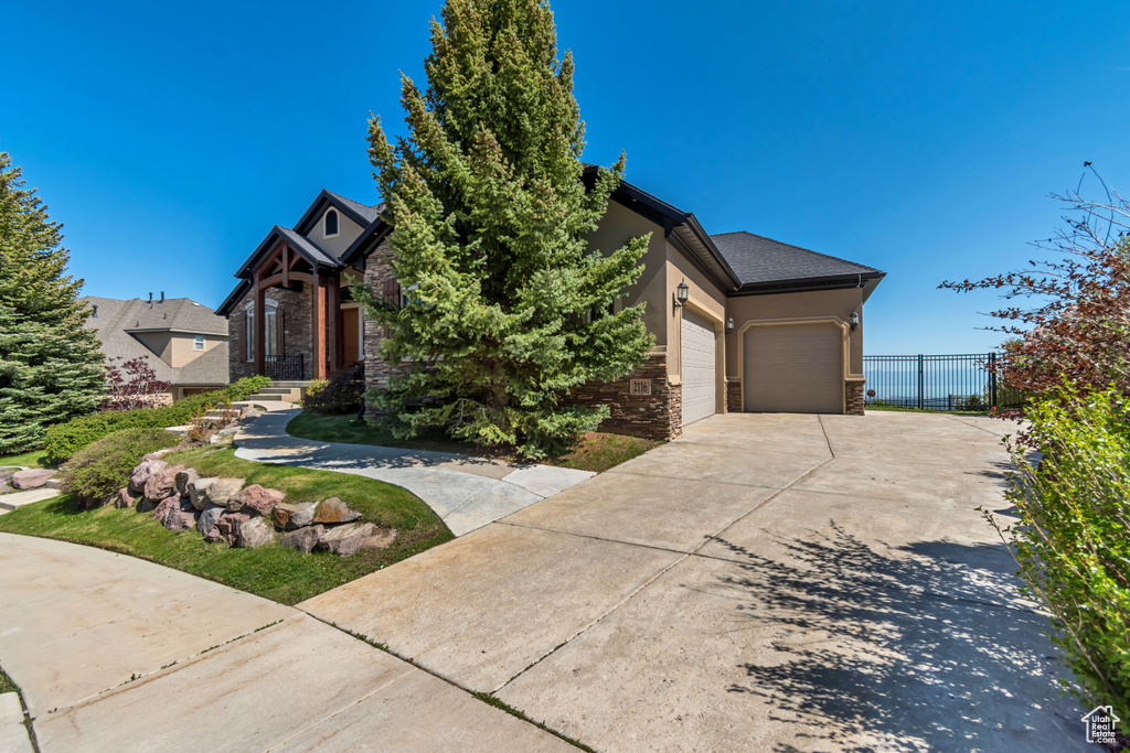 View of property hidden behind natural elements with a garage, driveway, stone siding, and stucco siding