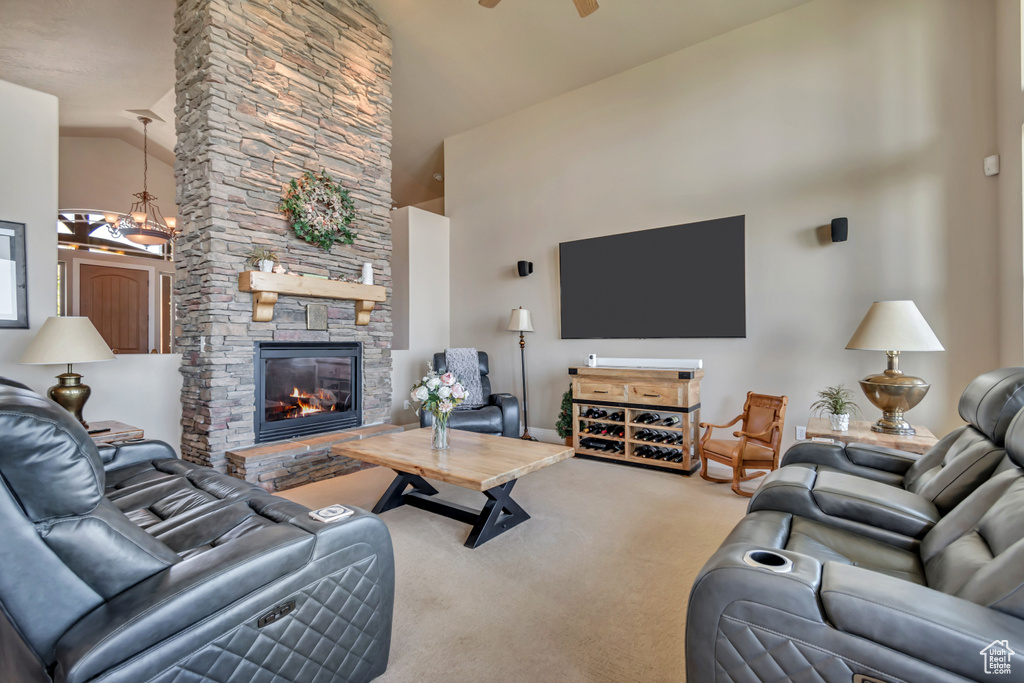 Carpeted living room featuring high vaulted ceiling, a chandelier, a stone fireplace, and ceiling fan