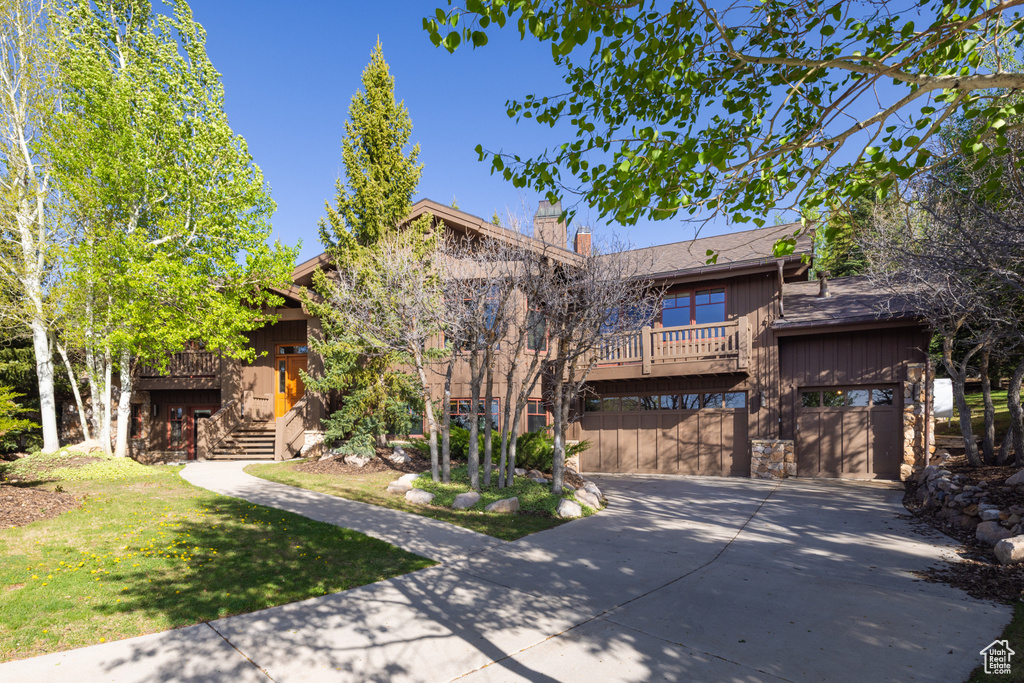 View of front of property with driveway, an attached garage, a chimney, a front lawn, and stone siding