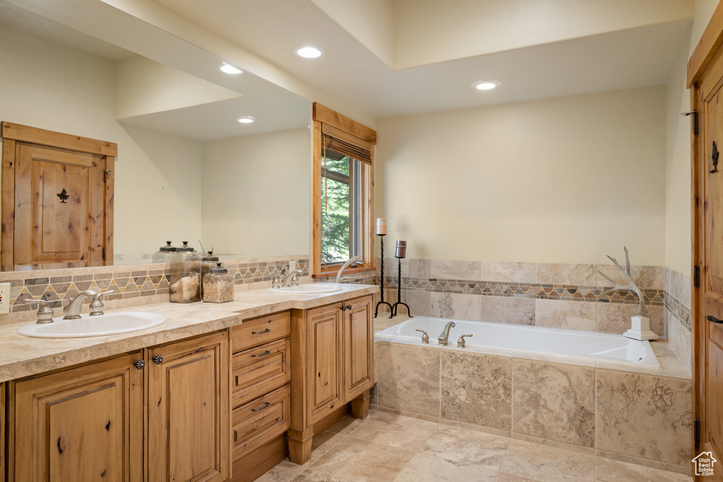 Bathroom featuring recessed lighting, a bath, double vanity, and backsplash