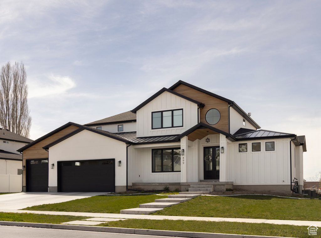 Modern inspired farmhouse with a standing seam roof, french doors, a front lawn, a garage, and concrete driveway