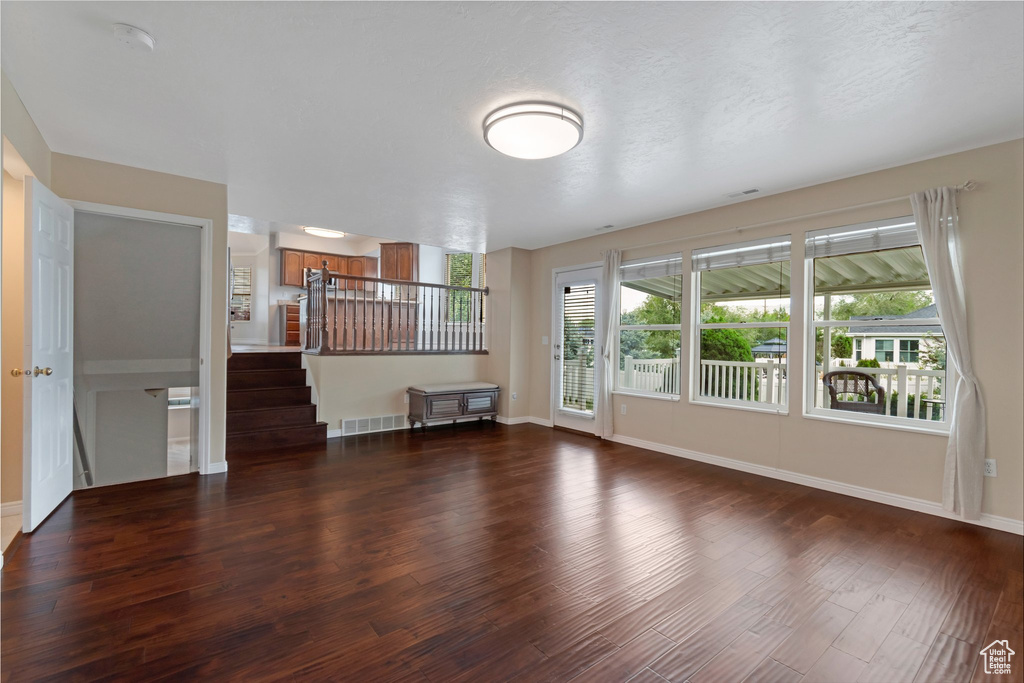 Unfurnished living room featuring wood finished floors, plenty of natural light, baseboards, and stairs