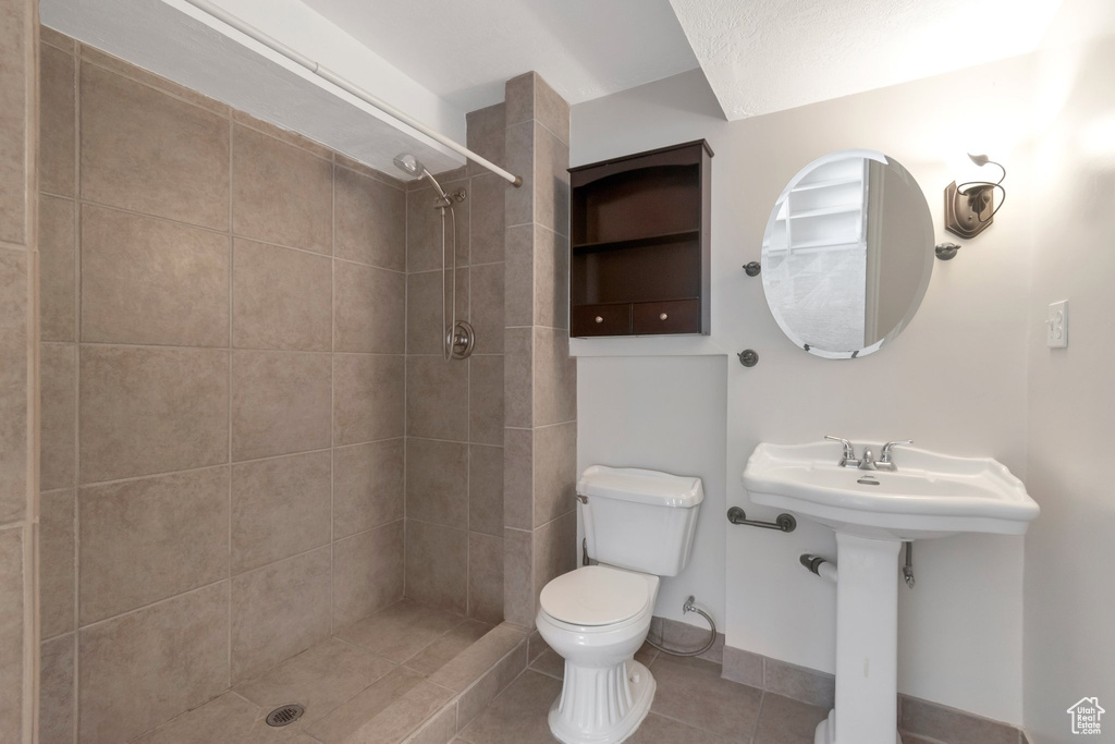 Full bath featuring toilet, tiled shower, tile patterned flooring, and baseboards