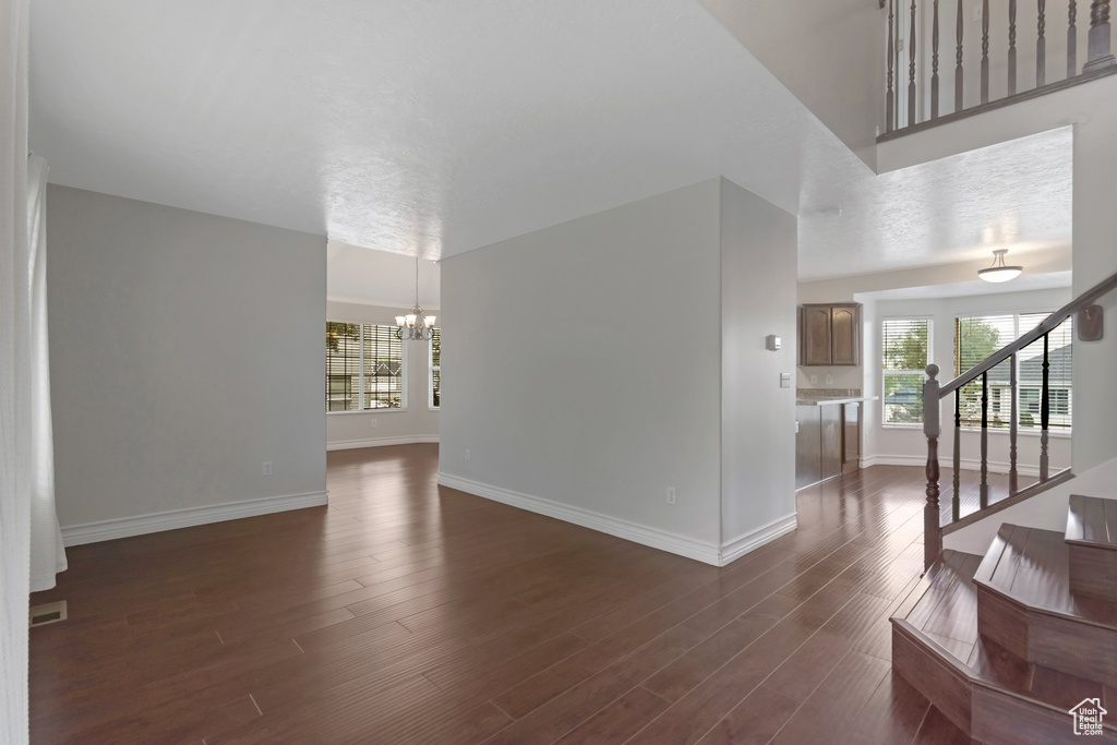 Unfurnished living room with a chandelier, baseboards, dark wood-style flooring, and stairway