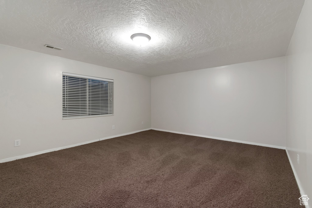 Unfurnished room with a textured ceiling, dark carpet, and baseboards