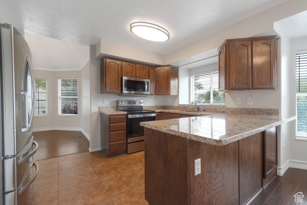 Kitchen with appliances with stainless steel finishes, a sink, a peninsula, baseboards, and brown cabinets