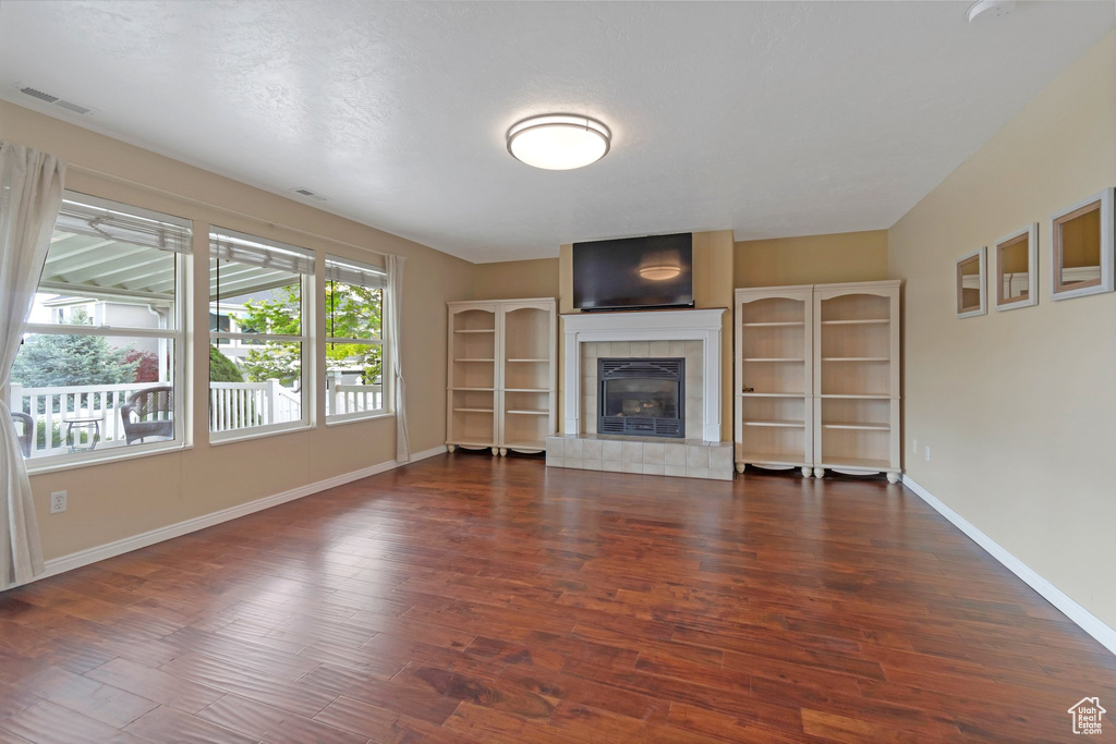 Unfurnished living room with wood finished floors, baseboards, and a tile fireplace