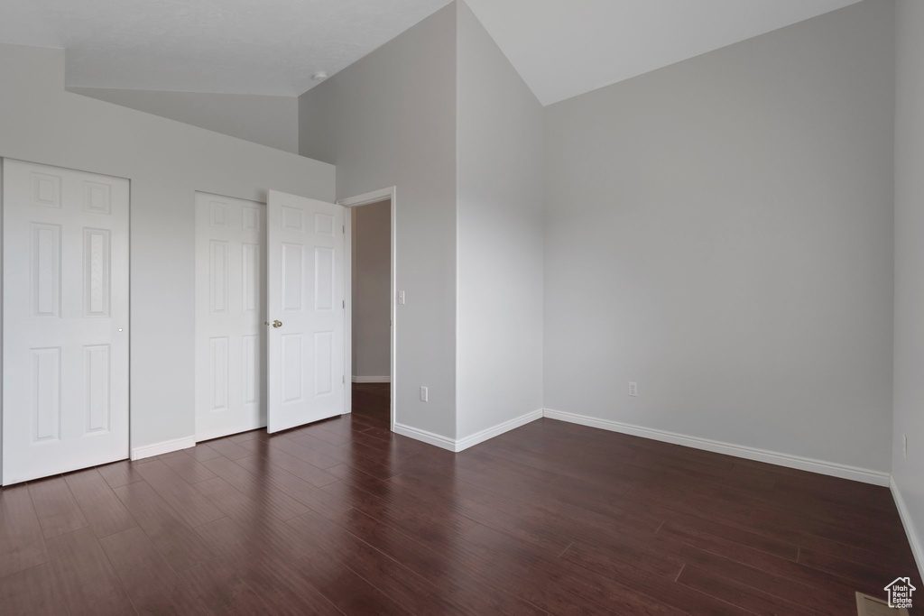 Unfurnished bedroom featuring lofted ceiling, baseboards, wood finished floors, and multiple closets