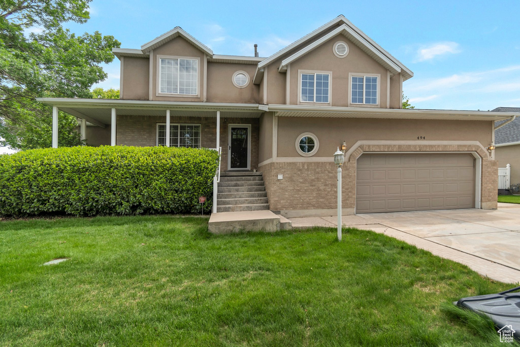 View of front of house with stucco siding, a front yard, concrete driveway, and brick siding