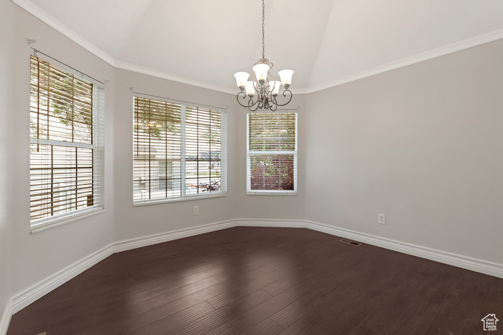 Empty room featuring a chandelier, healthy amount of natural light, dark wood finished floors, lofted ceiling, and baseboards